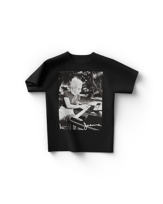 Black Lady Gaga t shirt front view featuring black and white photo of Lady Gaga playing piano with "Joanne" signature text